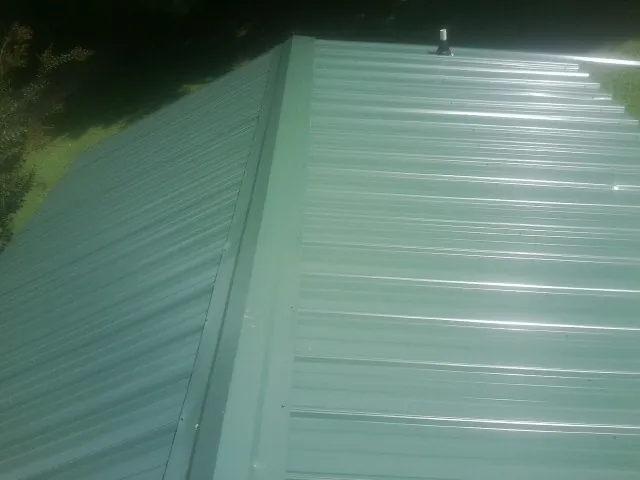 New green metal panels meeting at the ridge of a roof — Flat Roof Repair work by our crew in Mineola