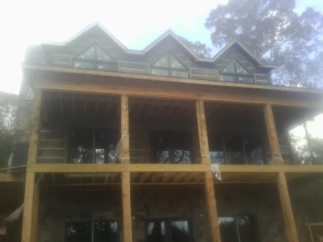 Dormers and porch framing on a large log home under construction — Roof Coating work by our crew in Mineola