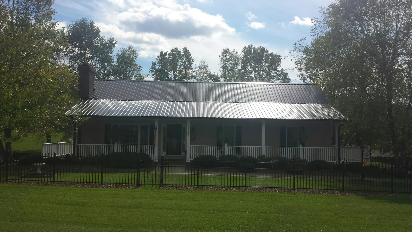 Gray metal roof on a brick ranch with a full width front porch — Gutter Guard Installation work by our crew in Mineola