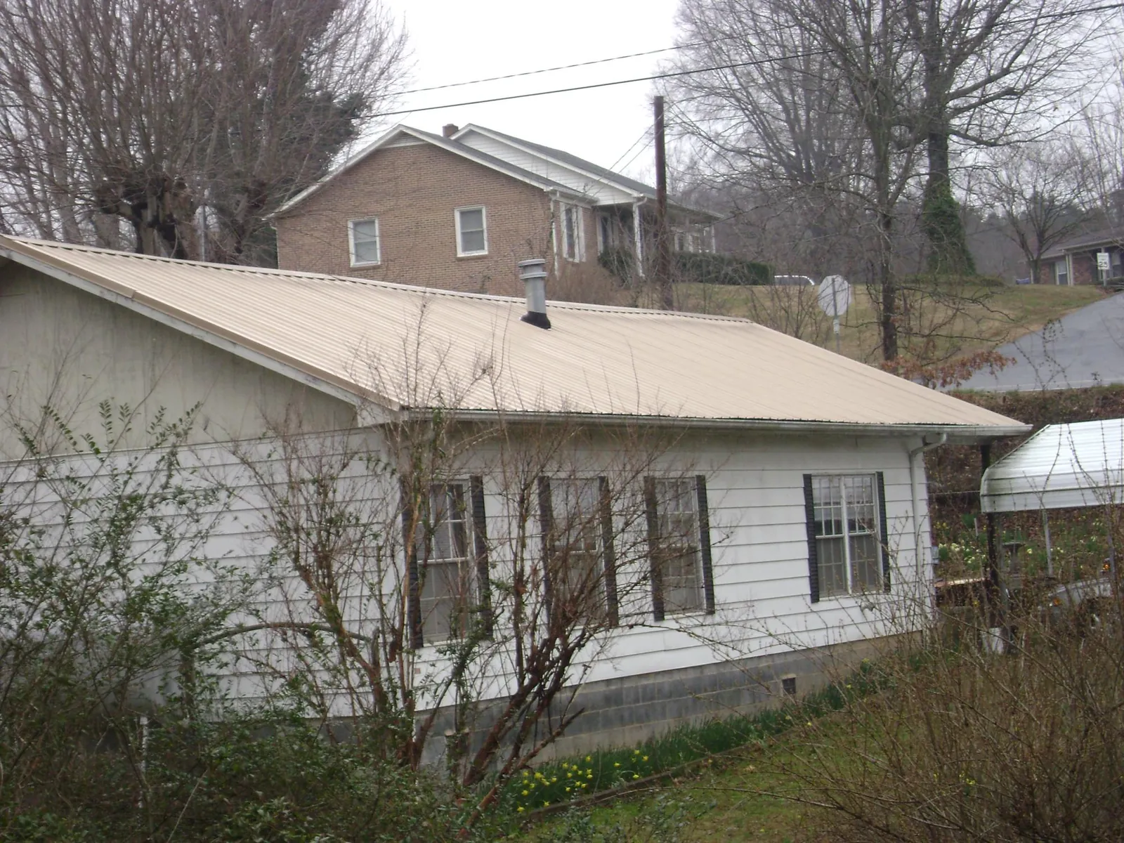 Tan metal roof on a white sided house set into a hillside — Commercial Roofing by Roofing Brothers in Mineola